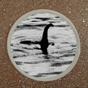 Può includere: Una fotografia in bianco e nero di una grande creatura serpentina nell'acqua. La creatura ha un collo lungo e una piccola testa. La foto è granulosa e sfocata, il che suggerisce che è stata scattata molto tempo fa.