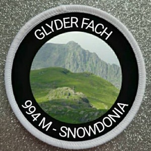 Könnte beinhalten: Runder weißer Patch mit schwarzem Rand und weißem Text. Der Text lautet "Glyder Fach 994 M - Snowdonia". Der Patch zeigt ein Foto einer Bergkette.