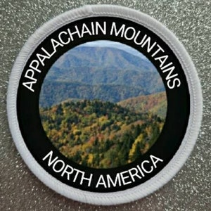 Może przedstawiać: Okrągła naszywka z widokiem na Góry Appalachów w Ameryce Północnej. Naszywka ma czarną obwódkę z białym napisem: "APPALACHIAN MOUNTAINS" i "NORTH AMERICA". Środek przedstawia krajobraz górski.