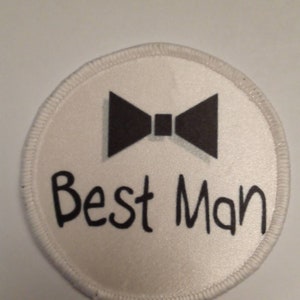 Può includere: Toppa circolare bianca con un papillon nero e il testo "Best Man" in nero.