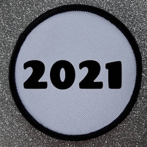 Könnte beinhalten: Runder weißer Patch mit schwarzem Rand und der Jahreszahl 2021 in Schwarz gedruckt.