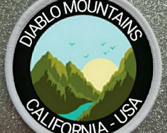 Peut inclure: Écusson rond blanc avec du texte noir et un graphique d'une chaîne de montagnes avec une rivière et un soleil. Le texte indique "Diablo Mountains California - USA".