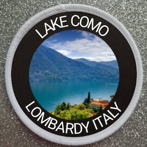 Könnte beinhalten: Runder weißer Patch mit schwarzem Rand und einem Foto des Comer Sees, Lombardei, Italien. Der Text "LAKE COMO" befindet sich oben auf dem Patch und "LOMBARDY ITALY" unten.