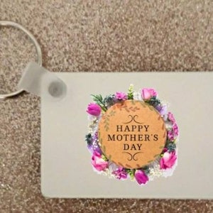 Könnte beinhalten: Weißer rechteckiger Schlüsselanhänger mit einem Blumendesign und dem Text "Happy Mother's Day" auf einem braunen Kreis.