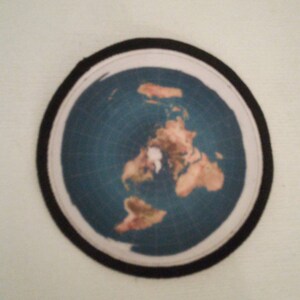 May include: A round, flat, blue and brown map of the world with a black border. The map is a flat-earth projection.