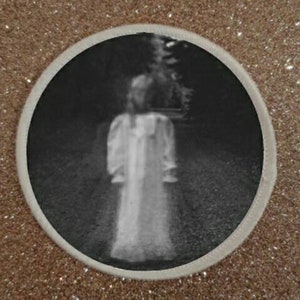 Può includere: Una fotografia in bianco e nero di una figura con un vestito bianco in piedi in un'area boscosa buia.