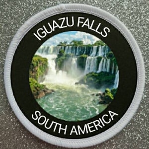 Könnte beinhalten: Ein weißer runder Patch mit schwarzem Rand und weißem Text, der "Iguazu Falls South America" lautet. Die Mitte des Patches zeigt ein Foto der Iguazu-Wasserfälle, einer Reihe von Wasserfällen in Südamerika.