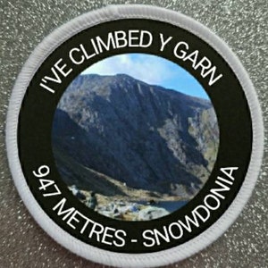 Może przedstawiać: Okrągła biała łatka z czarnym tekstem i zdjęciem góry. Tekst brzmi "I've Climbed Y Garn 947 Metres - Snowdonia".