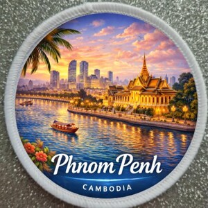 May include: Round patch featuring a scenic view of Phnom Penh, Cambodia, with a river, boats, and a golden temple. The image is set against a sunset sky with the city skyline in the background. The text "Phnom Penh" and "Cambodia" are displayed.