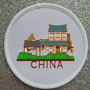 Può includere: Toppa rotonda bianca ricamata con un'illustrazione colorata di un edificio cinese con un tetto rosso e la parola "CINA" in lettere rosse.
