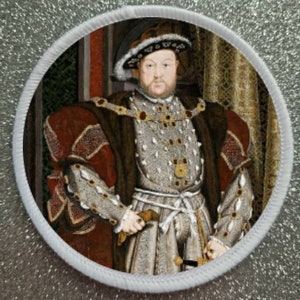 May include: A portrait of a man wearing a gold and white patterned robe with a red and gold patterned sash. He is wearing a crown and a fur-trimmed hat. The background is dark wood panelling with a gold and white patterned curtain.