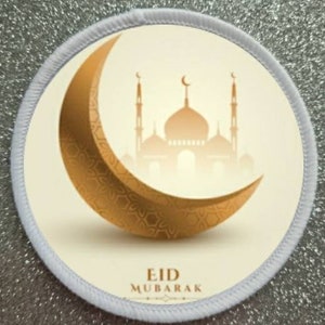 May include: A white circular patch with a gold crescent moon and a gold mosque silhouette. The text "Eid Mubarak" is printed in black at the bottom of the patch.