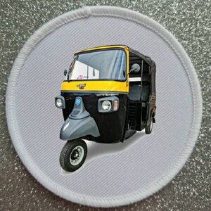 Puede incluir: Un auto-rickshaw negro y amarillo, también conocido como tuk-tuk, con un fondo blanco.