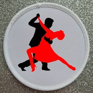 Può includere: Una toppa rotonda con bordo bianco e sfondo grigio. La toppa presenta una silhouette nera di un uomo e una silhouette rossa di una donna che ballano il tango. La donna indossa un vestito e tacchi alti.