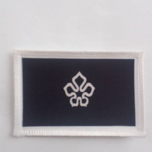 Könnte beinhalten: Ein schwarzer Patch mit einem weißen, stilisierten Blumendesign. Der Patch hat einen weißen Rand.