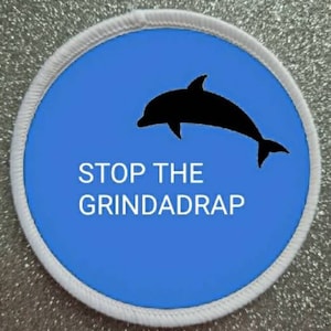 May include: A white round patch with a blue background and a black silhouette of a dolphin jumping out of the water. The text "STOP THE GRINDADRAP" is written in white letters below the dolphin.