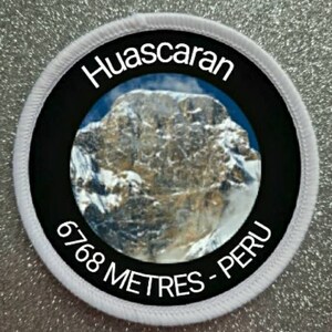 Puede incluir: Parche redondo blanco con borde negro y una foto de un pico de montaña cubierto de nieve. El texto "Huascaran 6768 Metres - Perú" está impreso en blanco sobre el borde negro.