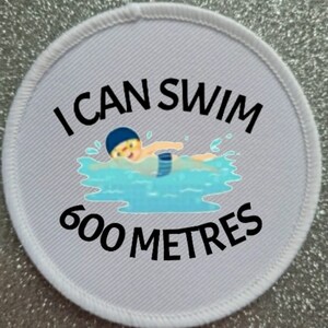 May include: White round patch with black text that reads "I can swim 600 metres". A cartoon illustration of a person swimming in blue water is in the center of the patch.