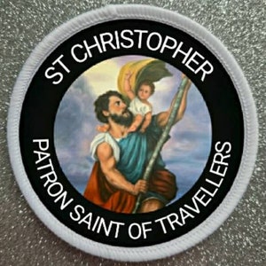 Könnte beinhalten: Runder weißer Aufnäher mit schwarzem Text und einem bunten Bild des Heiligen Christophorus, der ein Kind trägt. Der Text lautet "St Christopher Patron Saint of Travellers".