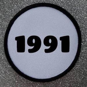Könnte beinhalten: Runder weißer Patch mit schwarzem Rand und der Jahreszahl 1991 in Schwarz gedruckt.