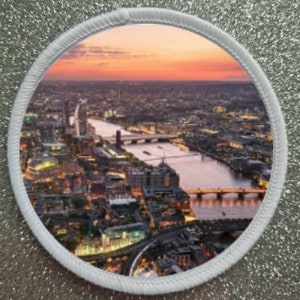 Peut inclure: Vue aérienne de Londres au coucher du soleil, montrant la Tamise, des ponts et des bâtiments. Les lumières de la ville sont visibles au loin.
