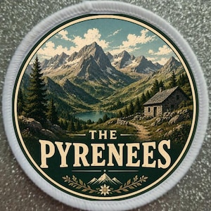 Puede incluir: Un parche bordado circular con una ilustración paisajística de los Pirineos, un lago y una cabaña de piedra. El texto THE PYRENEES está impreso en letras color crema en la parte inferior, acentuado por un pequeño icono de montaña y flor.