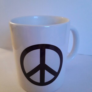Może przedstawiać: Biały kubek ceramiczny z czarnym symbolem pokoju.