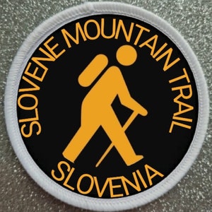 May include: A white circular patch with black and orange text and a graphic of a hiker with a backpack and walking stick. The text reads "Slovenia Mountain Trail Slovenia".