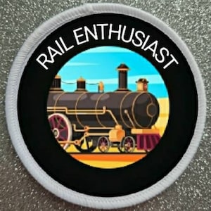 Peut inclure: Un écusson circulaire blanc avec du texte noir qui dit "RAIL ENTHUSIAST" autour d'un cercle noir avec une illustration colorée d'une locomotive à vapeur vintage.