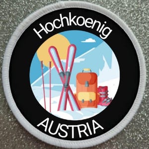 Könnte beinhalten: Ein weißer und schwarzer runder Patch mit dem Text "Hochkoenig Austria" in weiß. Der Patch zeigt eine Cartoon-Illustration einer verschneiten Berglandschaft mit Skiern, Stöcken, einem Rucksack und Skischuhen.