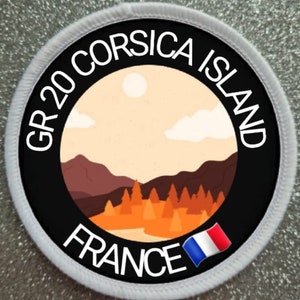 Könnte beinhalten: Ein schwarzer und weißer runder Patch mit weißem Text, der "GR 20 CORSICA ISLAND FRANCE" lautet. Der Patch zeigt eine Grafik einer Bergkette mit einem Fluss und Bäumen im Vordergrund. Eine kleine französische Flagge befindet sich in der unteren rechten Ecke.