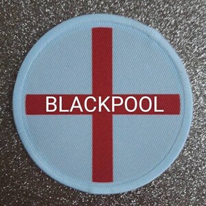 Pode incluir: Um remendo redondo branco e vermelho com uma cruz vermelha e a palavra "BLACKPOOL" em letras brancas.