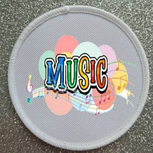 Op de afbeelding: Witte ovale stoffen patch met een kleurrijk muziekontwerp. Het woord "MUSIC" staat in regenboogkleuren met een witte omtrek. Het ontwerp bevat muzieknoten en swirls.