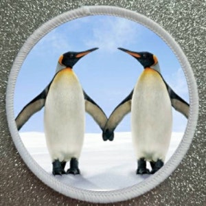 May include: Two penguins standing on snow, facing each other, with their wings outstretched and holding each other's flippers. The penguins are white with black markings on their heads and backs. The background is a blue sky.