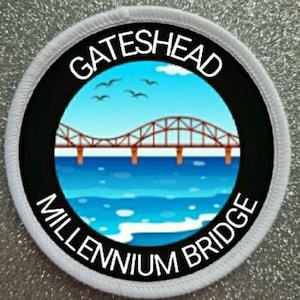 Può includere: Toppa rotonda con il Gateshead Millennium Bridge. Il ponte marrone si staglia sull'acqua blu. La toppa ha un bordo nero e bianco con le scritte "GATESHEAD" e "MILLENNIUM BRIDGE".