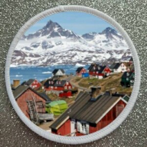May include: A colorful patch with a scenic view of a snow-capped mountain range and a small village with red houses. The village is nestled in a valley with a body of water in the foreground.