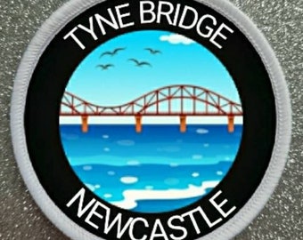 May include: A white circular patch with black text and a black circle in the center. The text reads "TYNE BRIDGE NEWCASTLE". The black circle contains a cartoon image of a red bridge over a blue body of water with white waves.