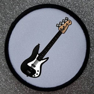 Peut inclure: Une guitare basse noire et blanche sur un fond bleu clair. La guitare a un corps noir et un pickguard blanc. La guitare a six cordes et une tête noire.