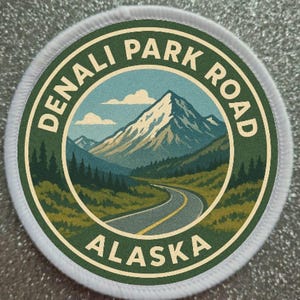 May include: Circular patch with a scenic illustration of Denali Park Road in Alaska. The design features a winding road, mountains, and the text "DENALI PARK ROAD ALASKA" in a circular layout, with a white border.
