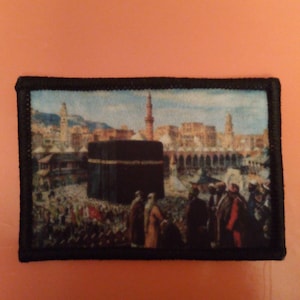 Puede incluir: Una imagen en blanco y negro de la Kaaba, un edificio en forma de cubo en La Meca, Arabia Saudita, rodeado de una multitud de personas. La Kaaba es un lugar sagrado en el Islam y es visitado por millones de peregrinos cada año.