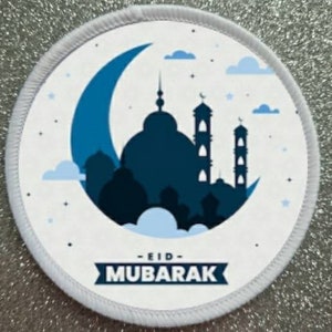 May include: White round patch with a blue crescent moon and a silhouette of a mosque with the text "Eid Mubarak" in a blue banner.