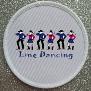 May include: White round patch with a blue border and the text "Line Dancing" in blue. The patch features a line of six cartoon figures in cowboy hats and boots, dancing. The figures are wearing blue and white shirts and pink and white skirts.