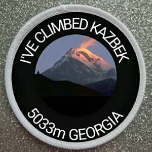 Könnte beinhalten: Runder weißer Patch mit schwarzem Text und einem Foto eines schneebedeckten Berggipfels. Der Text lautet "I've Climbed Kazbek 5033m Georgia".