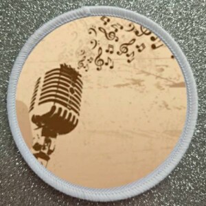 May include: A white round patch with a brown vintage microphone and musical notes on a beige background.