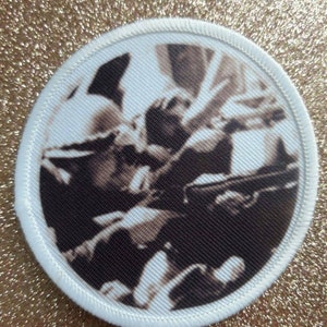 May include: A white round patch with a black and white image of a person playing a musical instrument. The image is in a circular frame with a white border.