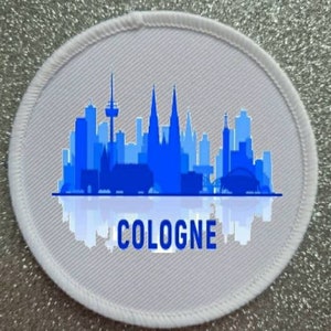 以下が含まれることがあります： コロンの街並みを青いシルエットで描いた白い丸いパッチ。ケルン大聖堂も描かれており、街並みの下に「COLOGNE」の文字が印刷されています。