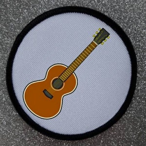 Könnte beinhalten: Eine braune Akustikgitarre mit einem hellen Holz Hals und goldenen Stimmwirbeln auf weißem Hintergrund. Die Gitarre befindet sich in einem Kreis mit schwarzem Rand.