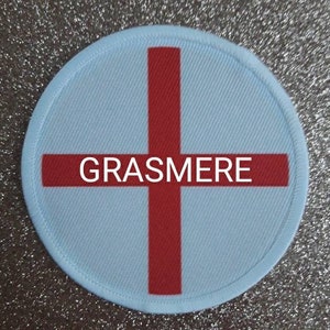 May include: A white round patch with a red cross and the word "GRASMERE" in the center.