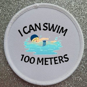 May include: White round patch with black text that reads "I can swim 100 meters". A cartoon illustration of a person swimming in a pool is in the center of the patch.