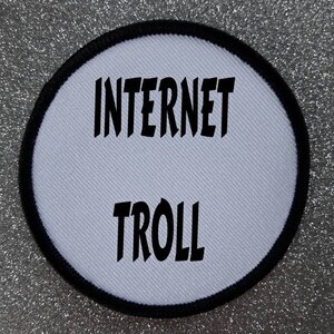 Könnte beinhalten: Runder weißer Patch mit schwarzen Nähten am Rand. Der Text "INTERNET TROLL" ist in Schwarz gedruckt.